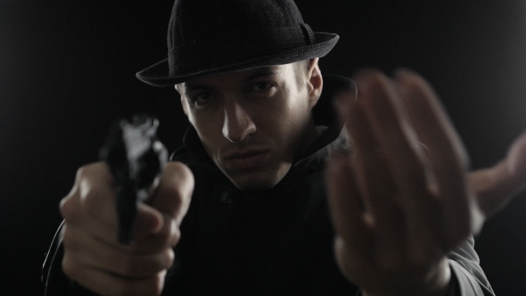 Gangster In a Hat And a Black Cloak. Mafioso Aiming a Gun At The Camera alt