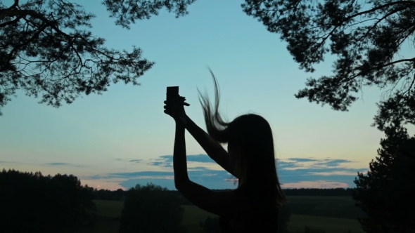 Silhouette Of a Young Woman Taking Selfie With Her Phone After Sunset