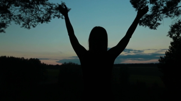 Happy Young Woman Silhouette Against Sky Lifts Hands Up In Air