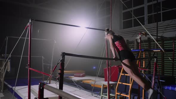 Sporty Female Gymnast is Performing Exercises on Uneven Bars in Gymnastic Hall at Evening Female alt