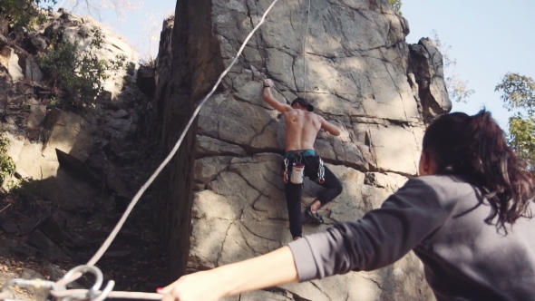 Man Climbing The Cliff With Woman Belaying Him alt