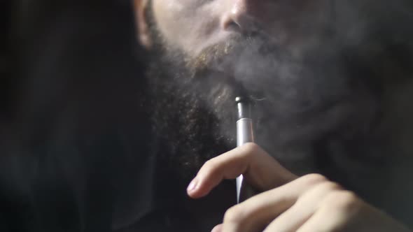 Young bearded man smokes a hookah and blow out smoke closeup on black background slowmotion