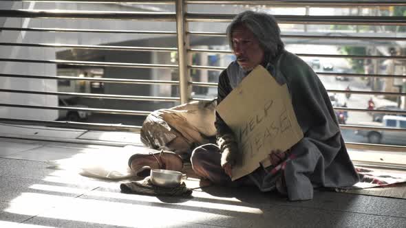 Homeless old man in dirty clothes sitting on the street and asking for help alt
