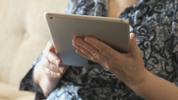 Old Woman Holding a Digital Tablet Sitting On Sofa