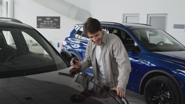 Happy Man Holding Keys of New Car and Smiling to Camera Enjoying Vehicle Purchase in Dealership alt
