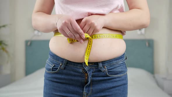 Young Woman Thinking of Loosing Weight Measuring Her Waist with Measuring Tape alt