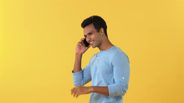 Handsome smiling young Indian man waving his hand while walking and talking on mobile phone