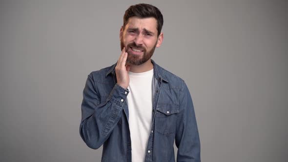 Caucasian man touching cheek and wincing in pain feeling terrible tooth ache, gingivitis