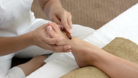 Therapist giving foot massage with stick to a woman in spa