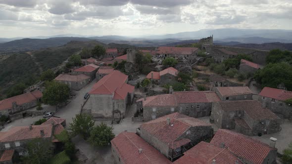 Drone flying over roofs of granite rural houses in Sortelha village with mountains in background