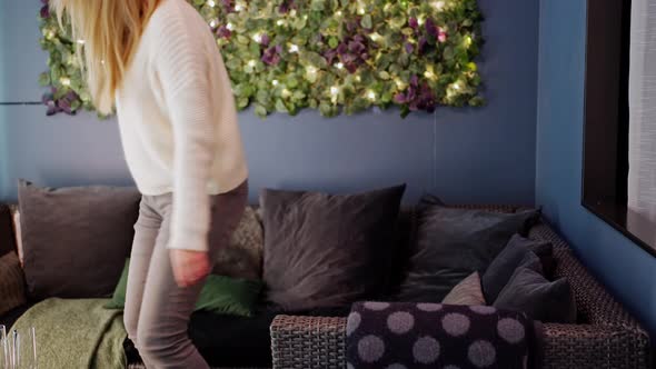 Woman Enters the Frame and Sits on a Gray Sofa with Her Arms Outstretched alt