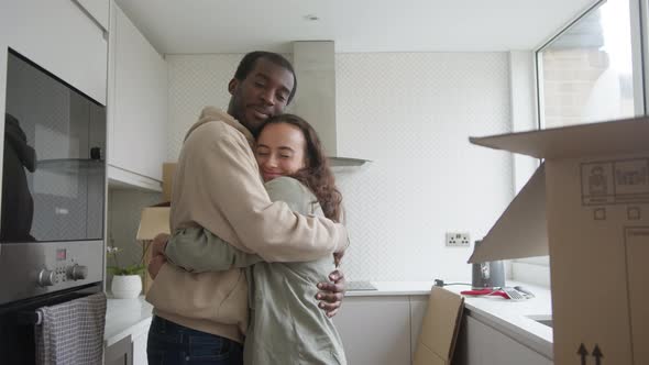 Young Couple In New Home Hugging As They Unpack Removal Boxes In Kitchen Together