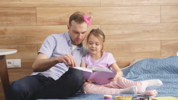 Family Father and Kid Girl Reading Book Fairytale Sitting on Bed at Home