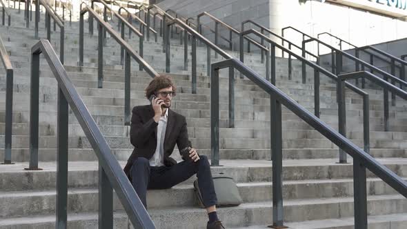 Businessman Sitting on Stairs Near Business Center Talking on the Phone alt