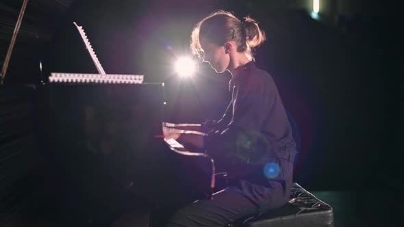 A young woman plays the piano energetically in the spotlight on the stage alt
