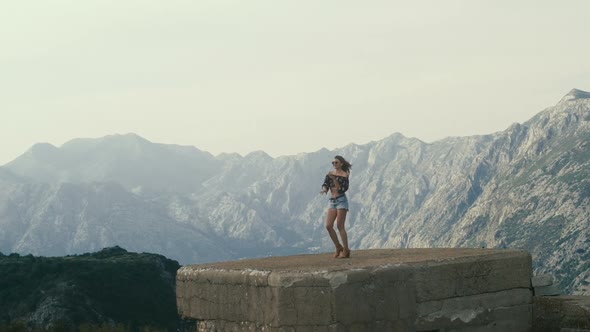 Young curly-haired woman in sunglasses on the background of the mountains alt