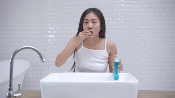 Daily routine concept. Young Asian woman gargling in the bathroom. 4k Resolution. alt