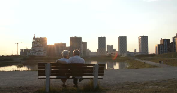 Silhouette of an Elderly Couple Sitting on a Bench Against the Backdrop of a Cityscape alt