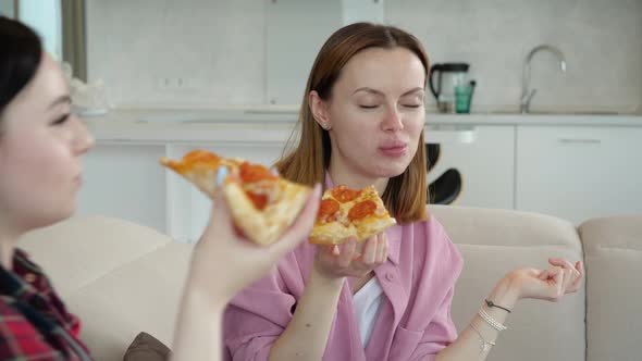 Two Young Girlfriend Girls Deliciously Eating Pizza and Talking Sitting at Home