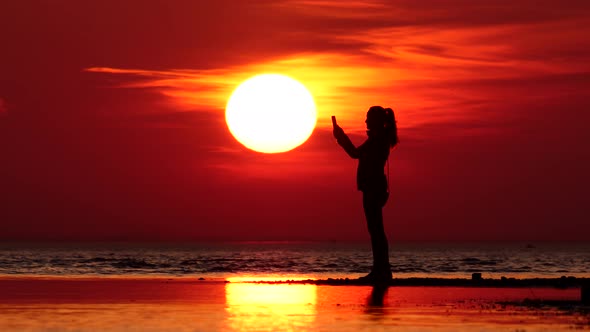 Woman silhouette at sunset, cool weather, sea shore, large sun disc on back