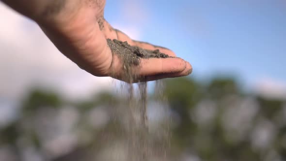 close-up hand grabs a handful of dry sand and lets it fall between his fingers alt