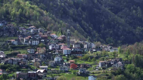 Remote Villadossola town with clock tower in green Italian Alp hillside; drone alt
