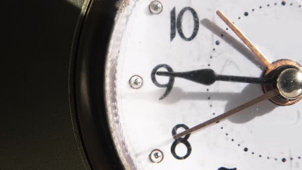 Close-up of an old mechanical table clock. The second hand runs across the white dial.