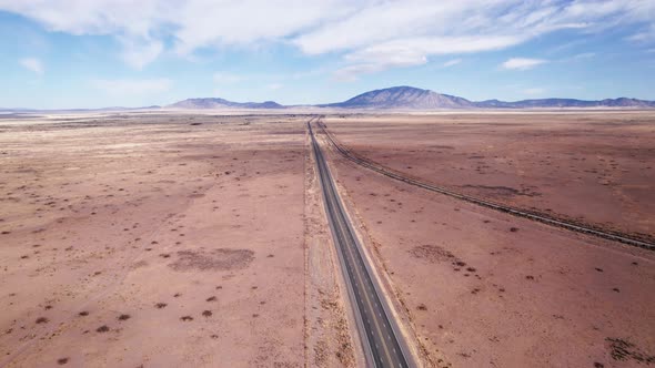 Drone shot flying straight over a desert highway and railroad track alt