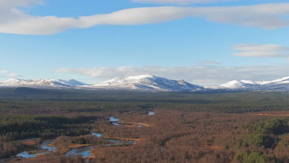 Parallax Drone Shot Of Snowcapped Swedish Mountains Surrounded By Alpine Forest And River. alt
