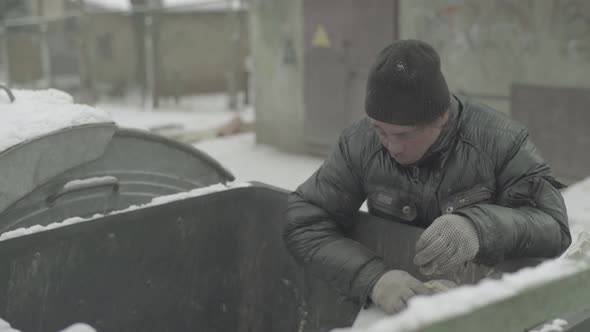 A Beggar Homeless Man Tramp Is Looking for Food in a Trash Can. Kyiv. Ukraine alt