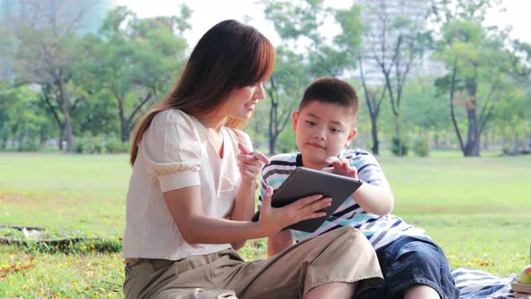 Asian family with two children sitting using a digital tablet together in public park
