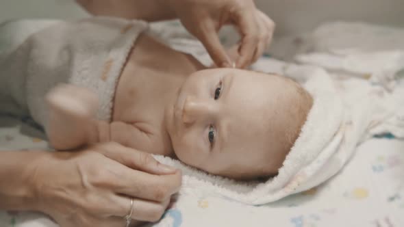 A Little Baby Lying in Bed and His Mother Cleaning His Ears alt
