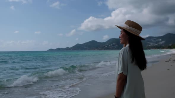 Slow motion of a young woman with hat standing and looking at the sea