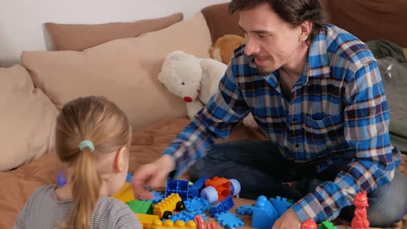 Dad and Daughter Play with Construction Set on Bed in Bedroom Indoors at Home
