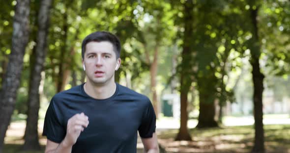 Adult Man Running Outdoor Using Wireless Earphones Listening to Music With Smartwatch