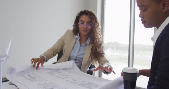 Biracial female architects talking and checking architects plans in modern office alt