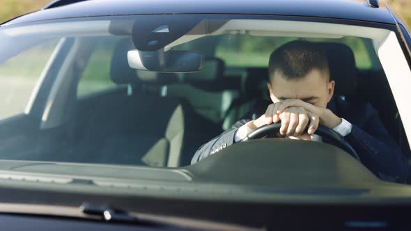 Exhausted Male Driver Holding Head in Steering Wheel While Sitting in Side Modern Luxury Car