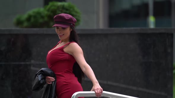 a Brunette with Long Hair and Big Breasts in a Red Dress with a Neckline and a Burgundy Cap Smiles alt