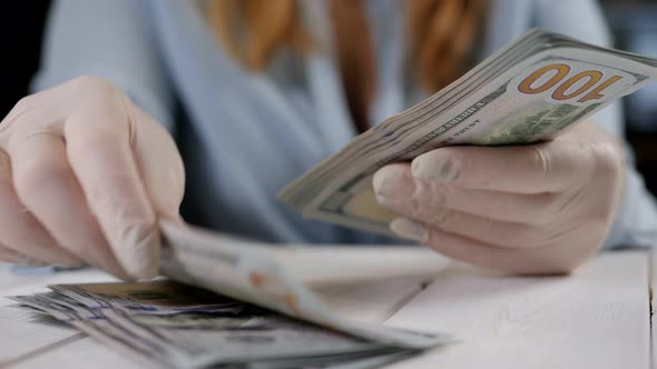 A Woman in Gloves Counting Hundreddollar Bills on a Light Wooden Background alt