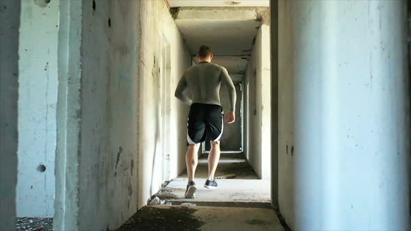 Tracking Shot of Anonymous Male Athlete Running in Dark Hallway of Derelict Building During Intense