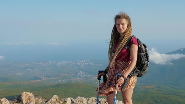 Girl with Backpack and Sticks Stands on Mountain alt