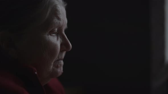 Slow Motion Handheld Shot of Old Woman Sitting Near Window and Thinking About Something