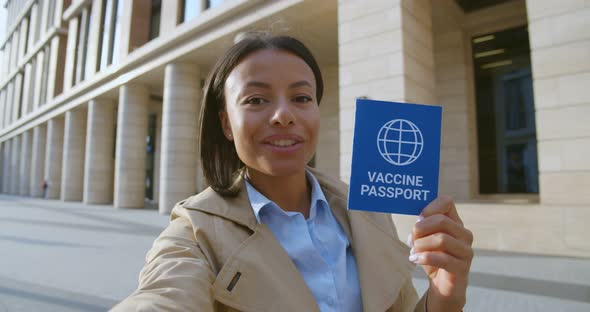 Afroamerican Female Traveler with Vaccination Passport Looking at Camera and Talking Outdoors alt