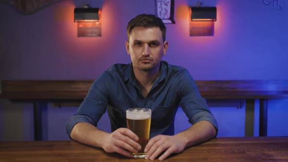 Portrait of a Happy Young Man in Glasses in Pub with Glass of Beer in Hand at Bar Counter