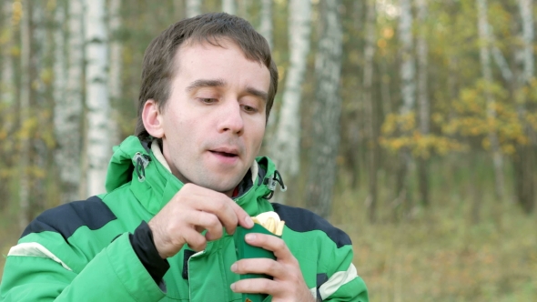 A Young Man an the Autumn Forest Eating French Fries. Warm Jacket and Beautiful Green Trees