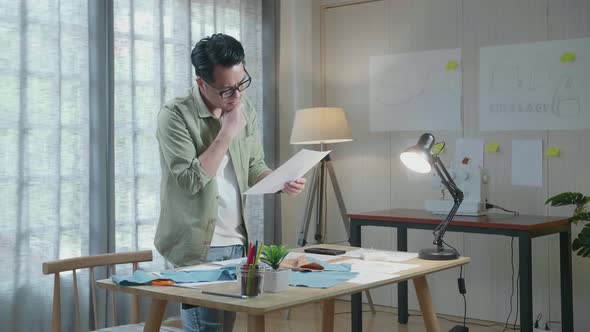 Side View Of Asian Man Designer With Fabric Thinking While Looking At The Layout Bond At The Office alt