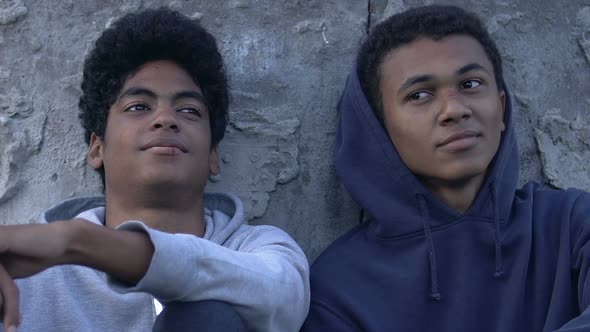 Two African-American homeless teen boys sitting on street alt
