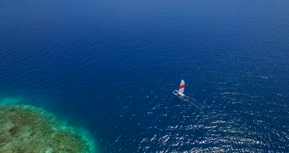 Aerial drone view of a man and woman sailing on a boat to a tropical island. alt