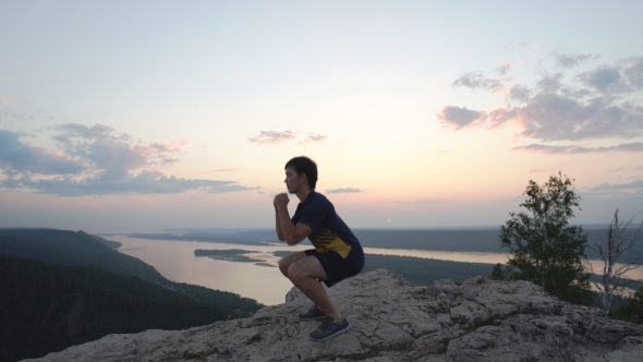 a Man Crouches On Top Of a Mountain alt