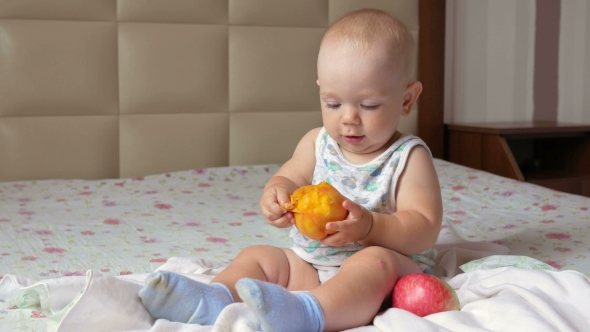 A Handsome Baby Eating a Peach On a Breakfast In Bed. He Tears Off a Piece And Puts In His Mouth